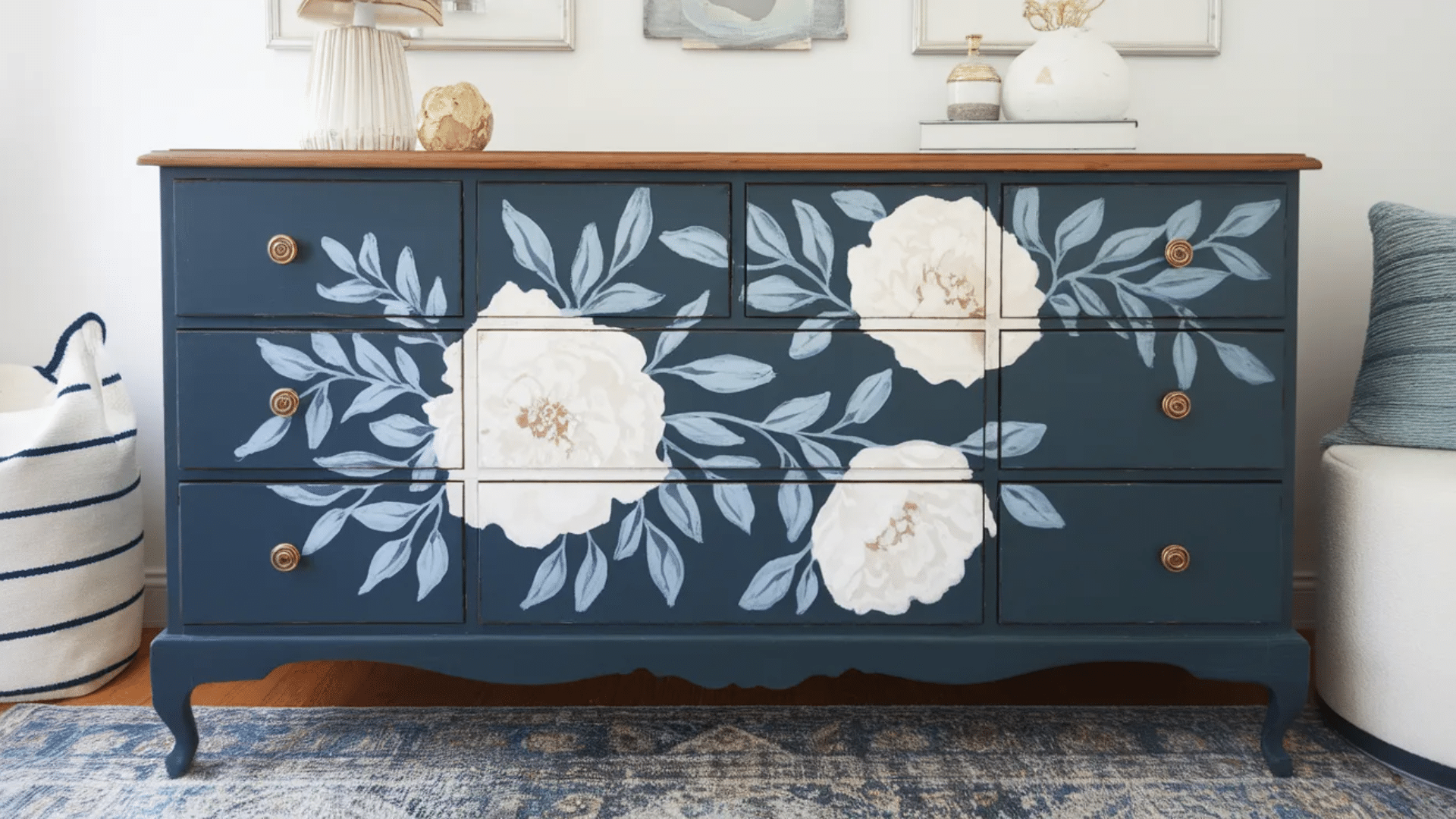 image features a beautifully painted floral design on a vintage dresser. The dresser has a rich navy blue base color, with large, soft white peonies and delicate blue-green leaves painted across t