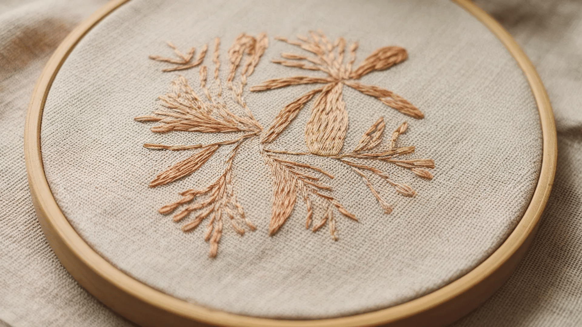 image showcases a delicate, hand-stitched embroidery of floral designs. The intricate stitching is done in soft, muted tones of peach and beige, giving the piece a natural, organic feel