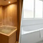 Wooden traditional Japanese soaking tub with potted fern next to modern white bathtub with towel