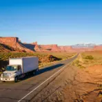 White truck driving on highway through red rock desert landscape under clear blue sky