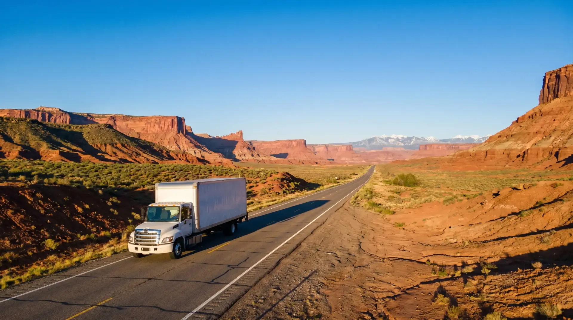White truck driving on highway through red rock desert landscape under clear blue sky