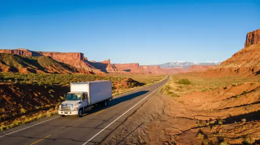 White truck driving on highway through red rock desert landscape under clear blue sky