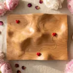 Wooden mountain sculpture with red heart decoration surrounded by pink peonies and gold rings on linen cloth