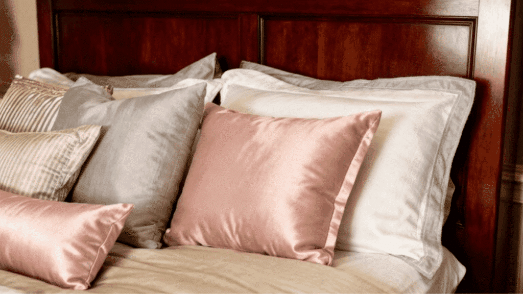 neatly arranged bed with soft satin and cotton pillows in neutral tones against a wooden headboard in cozy bedroom setting
