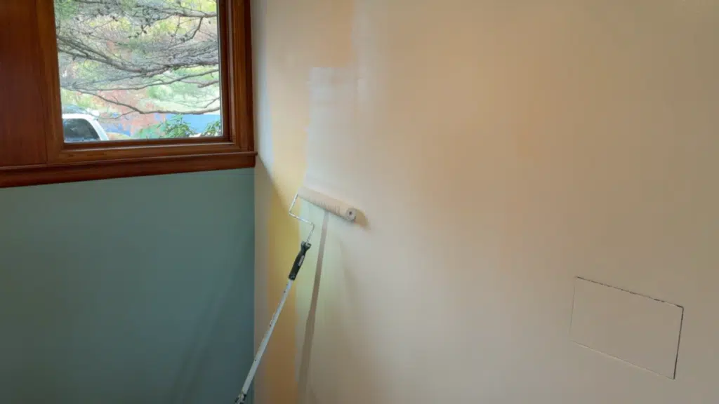 paint roller applying fresh coat on wall near window with natural light and visible trim