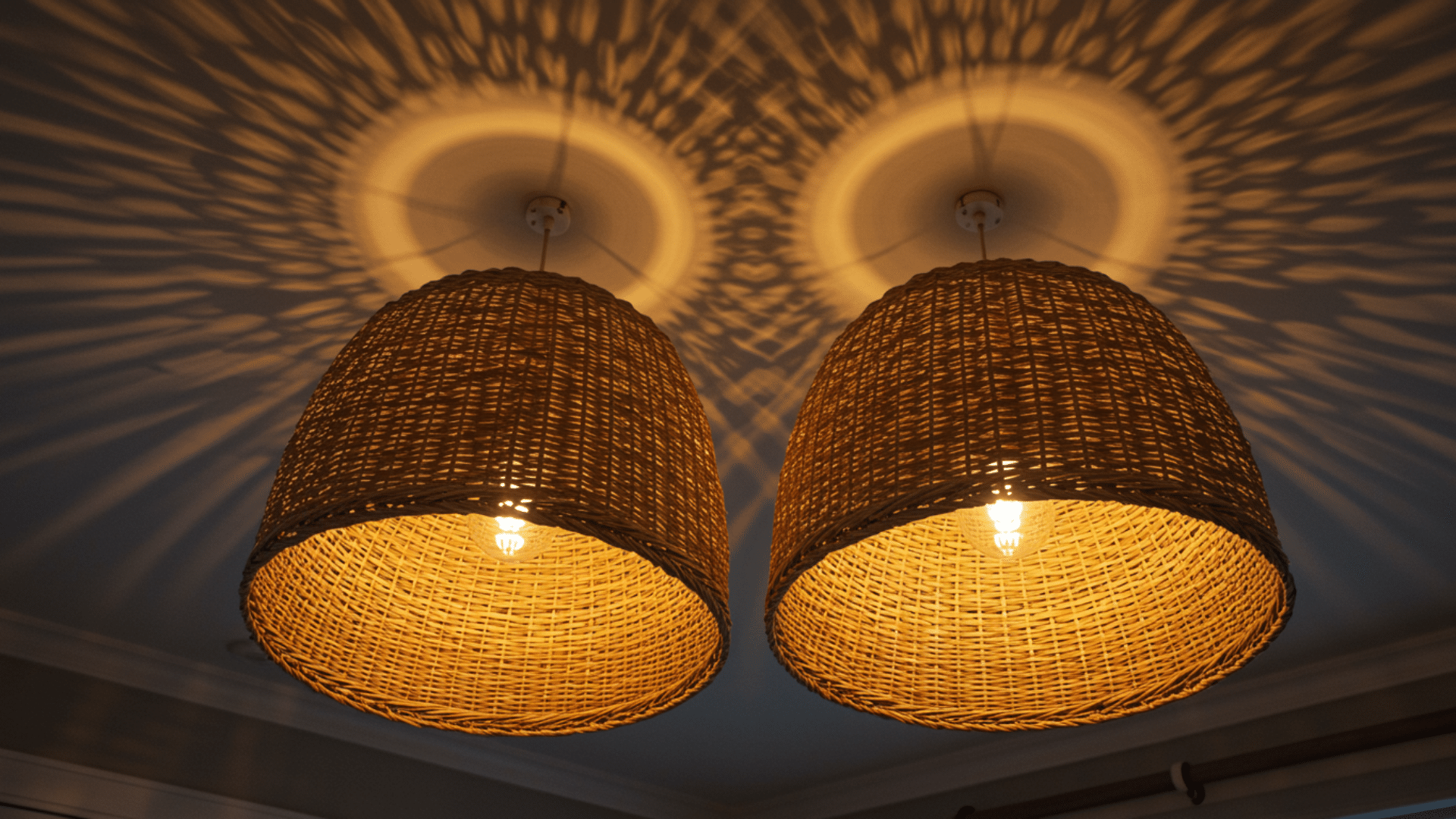pair of woven rattan pendant lights hanging from ceiling casting warm patterned shadows in circular shapes across the ceiling above