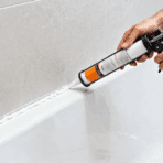 person applying silicone caulk along bathtub edge using caulking gun in modern bathroom, sealing joints neatly