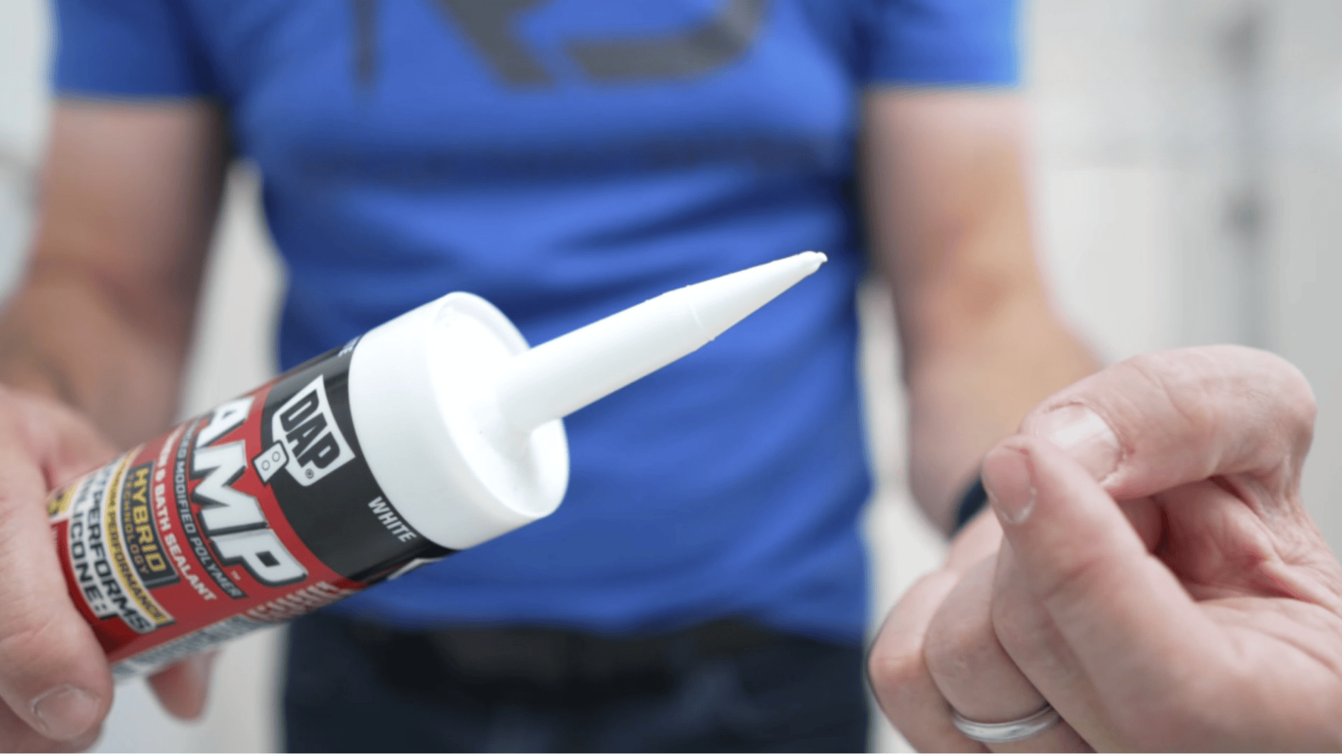 person holding caulk tube with nozzle close up showing white sealant ready for application in bathroom repair task (1)