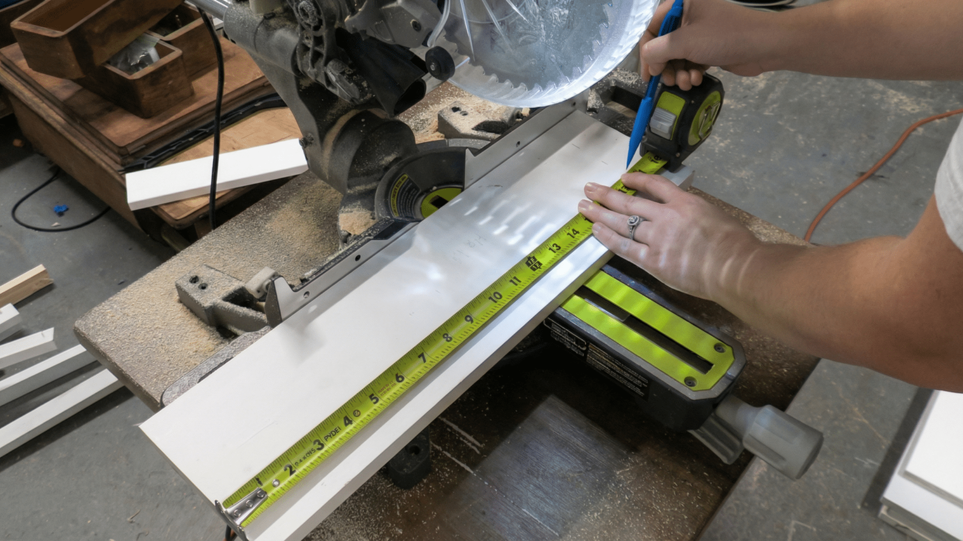 person measuring and marking a board with a tape measure before cutting it with a miter saw
