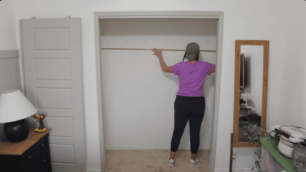 person measuring inside empty closet with tape measure stretched across wall, preparing layout for shelves and storage system installation