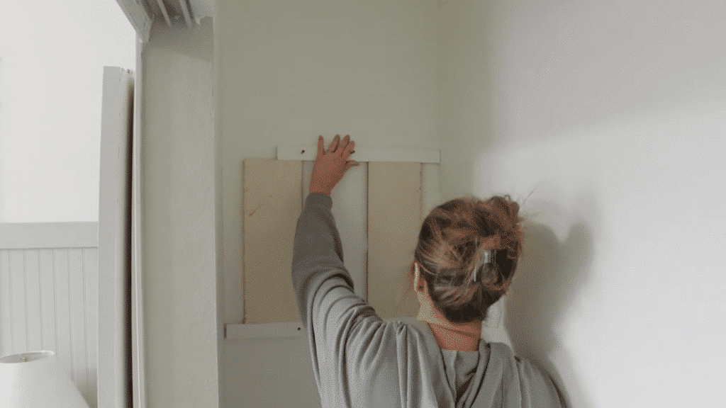 person positioning wooden support board on wall, aligning and pressing it into place before fastening for closet shelving structure