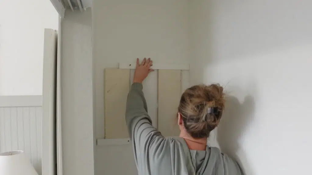 person positioning wooden support board on wall, aligning and pressing it into place before fastening for closet shelving structure