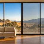 Beige sofa and potted plant beside large windows overlooking hills in a sunlit living room