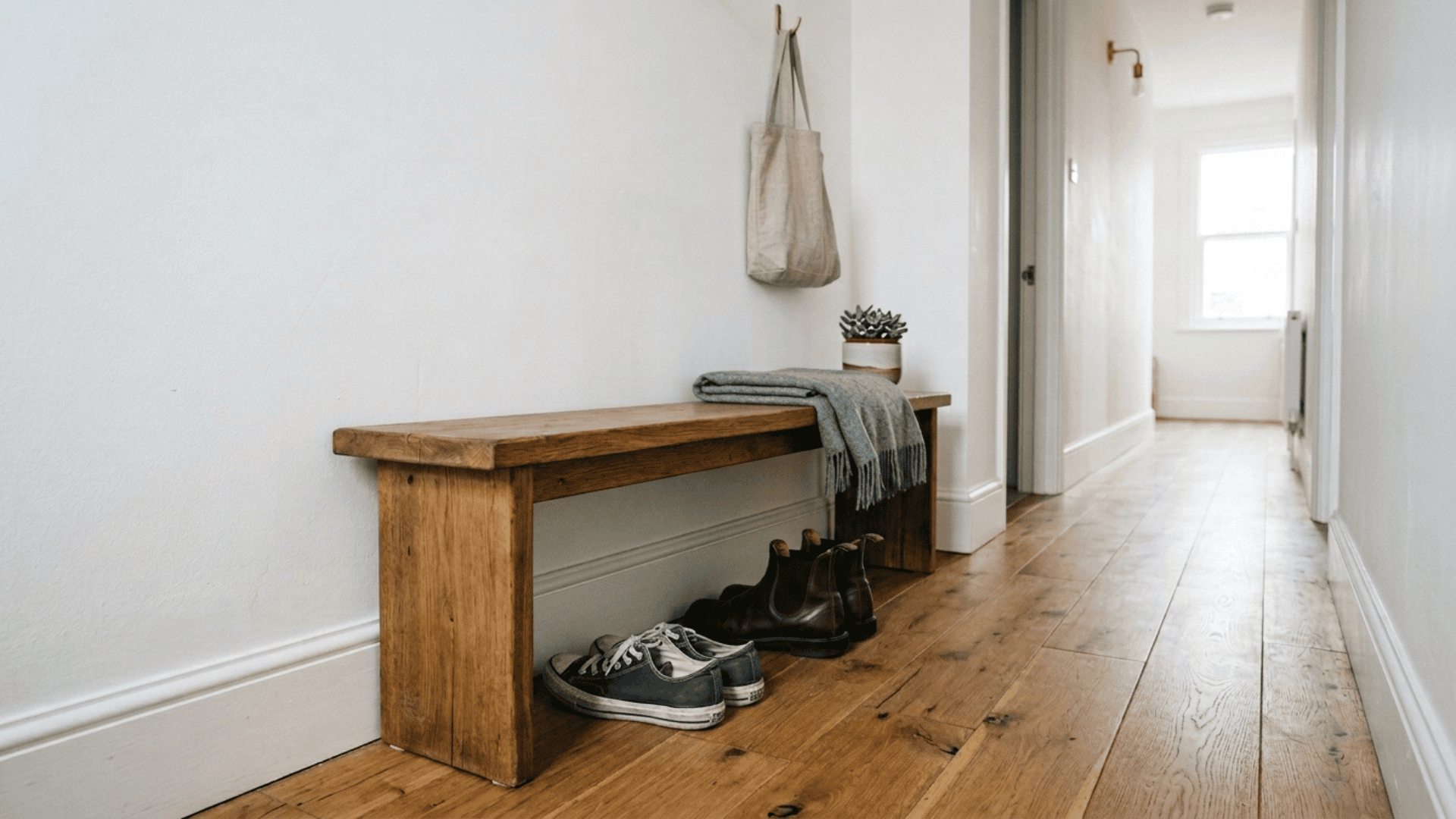 simple rustic wooden hallway bench with shoes stored underneath and a tote bag hanging on a wall hook above