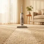 Cordless vacuum on beige carpet in sunlit living room with light sofa and potted plant