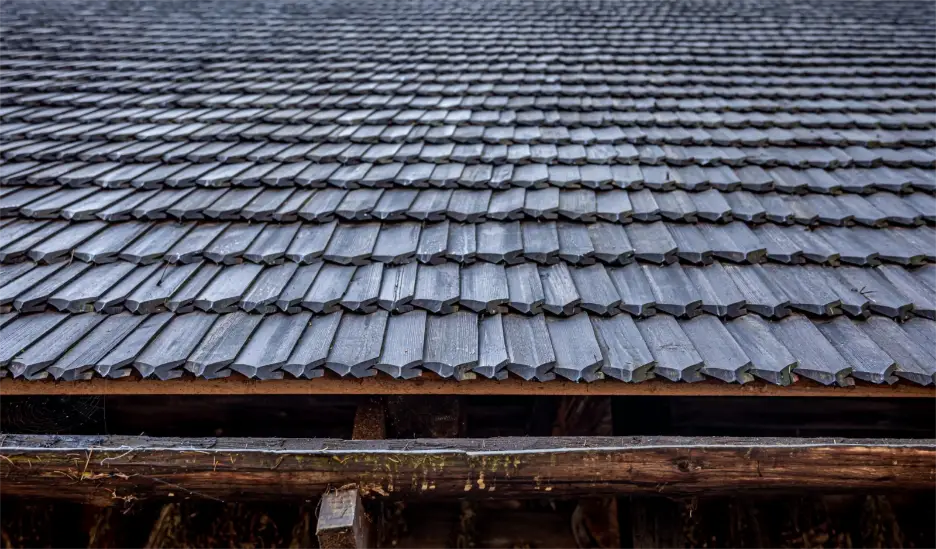 Wooden shingled roof with overlapping tiles on rustic structure in cool lighting