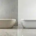 Two modern freestanding bathtubs with potted plants on a marble floor in a bright bathroom