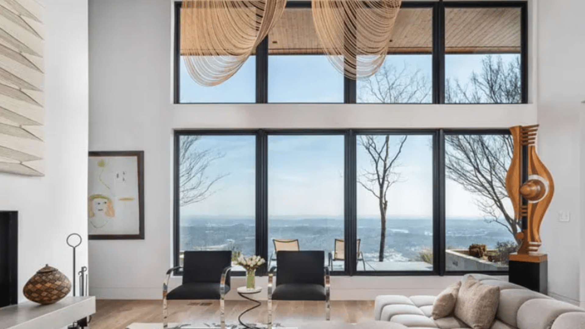 spacious modern living room with floor to ceiling windows, scenic outdoor view, lounge chairs, sofa, and minimalist decor