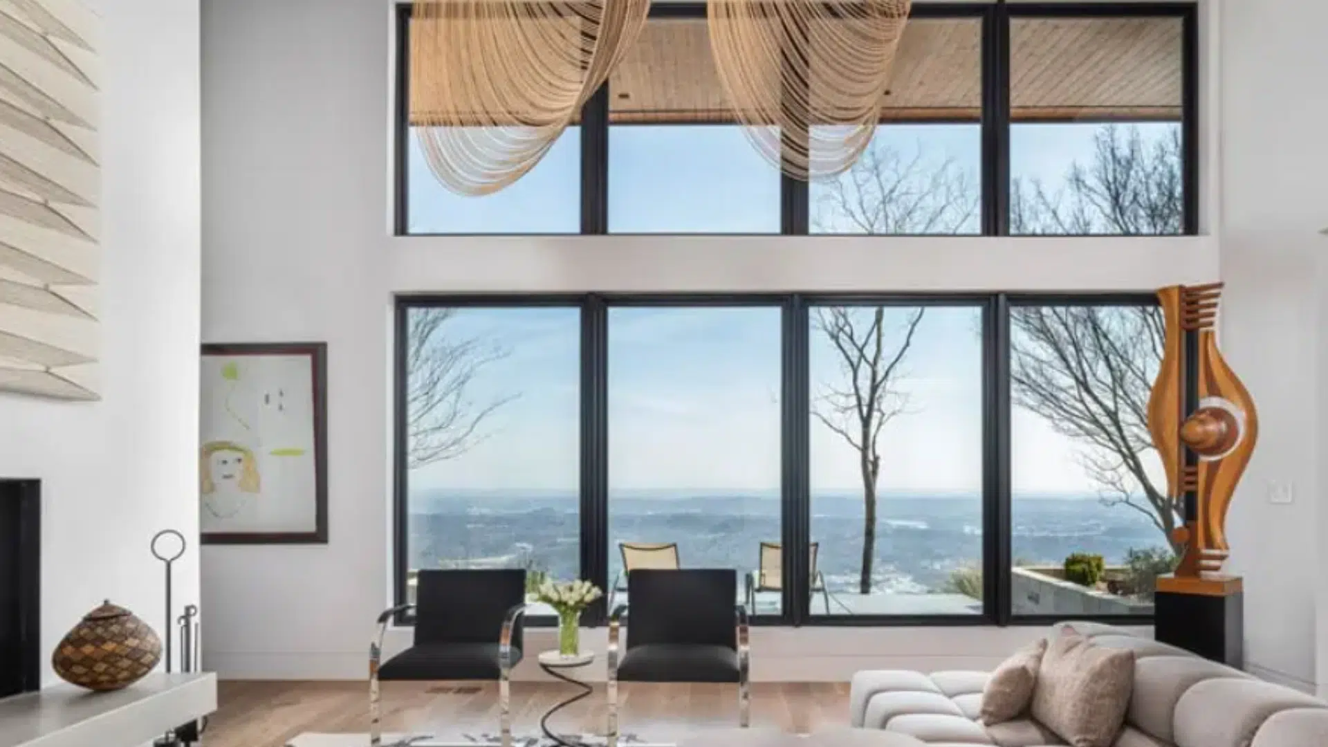 spacious modern living room with floor to ceiling windows, scenic outdoor view, lounge chairs, sofa, and minimalist decor