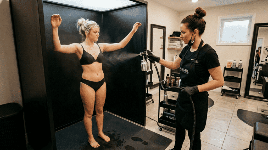 spray tan technician applying solution to a client's arm during a professional spray tan session in a salon