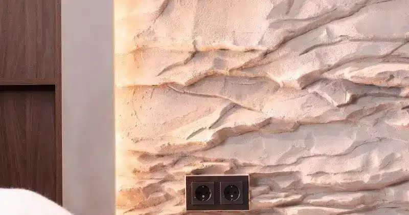 Textured plaster wall with layered design and brown electrical outlets in a softly lit interior