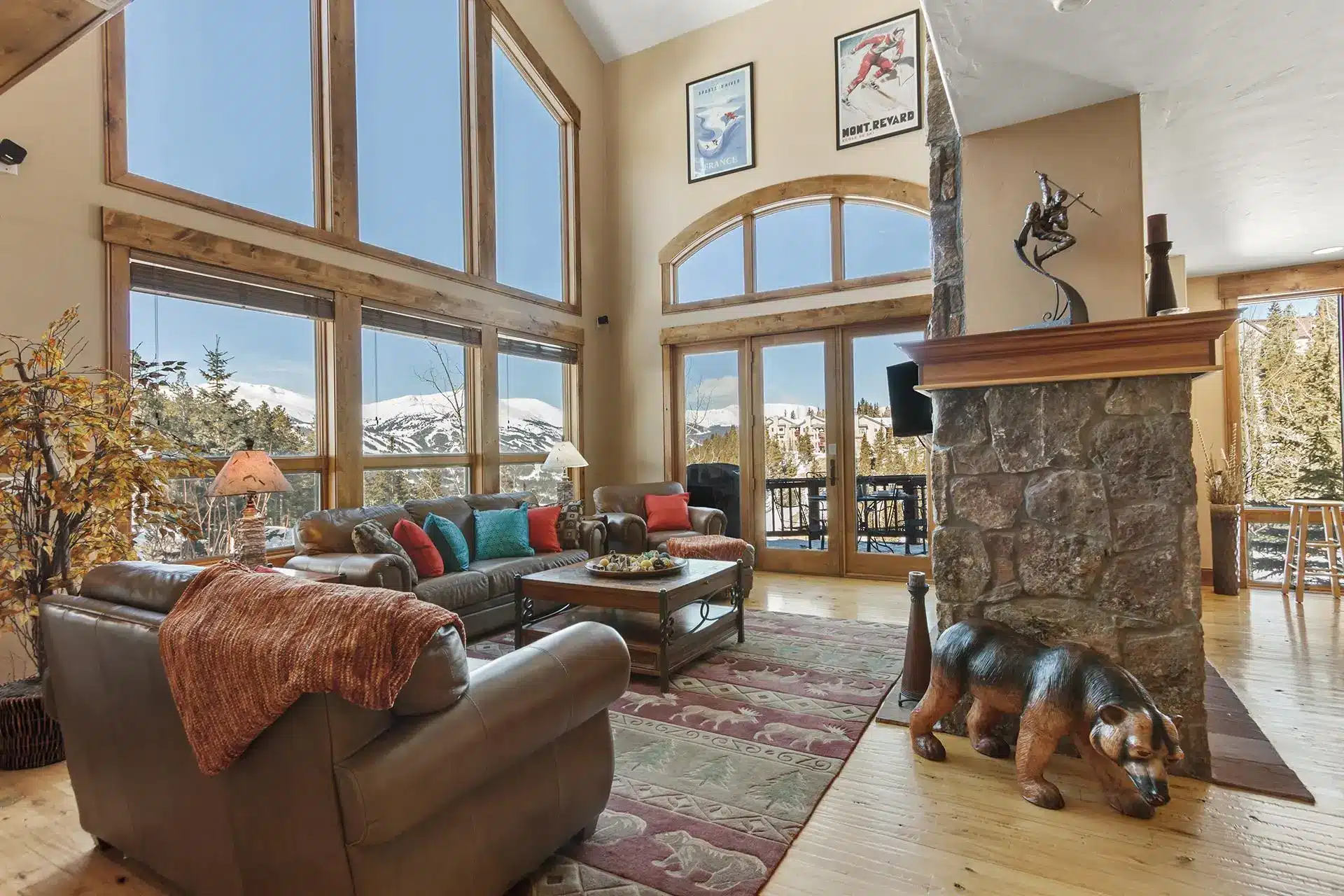 Cozy mountain cabin living room with large windows, leather sofas, and a stone fireplace