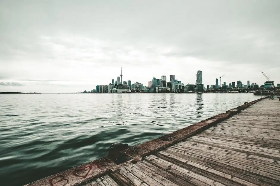 City skyline across a calm lake with wooden pier in foreground under cloudy sky