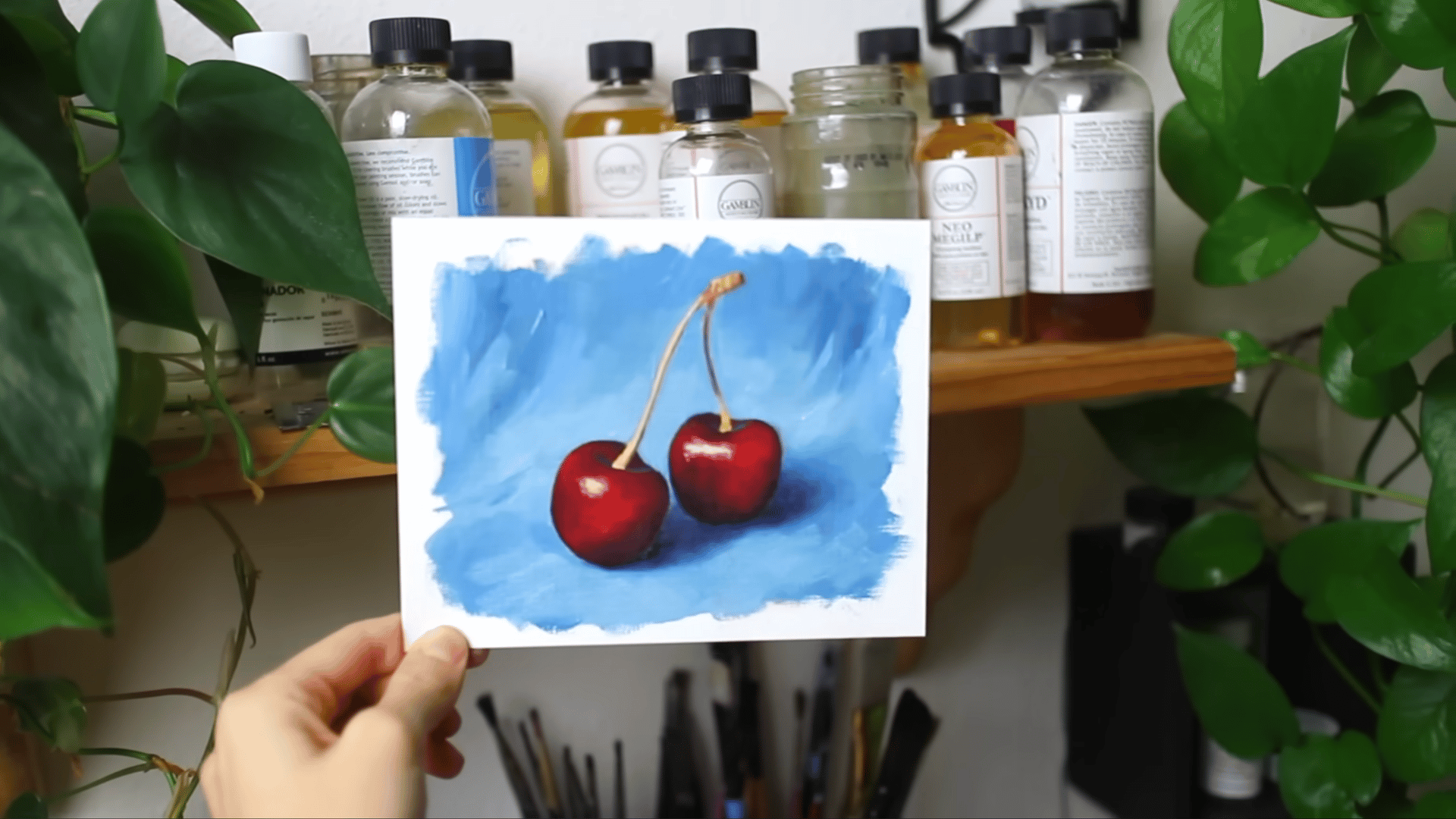 the completed oil painting of two red cherries on a blue background held up showing the finished result of the process