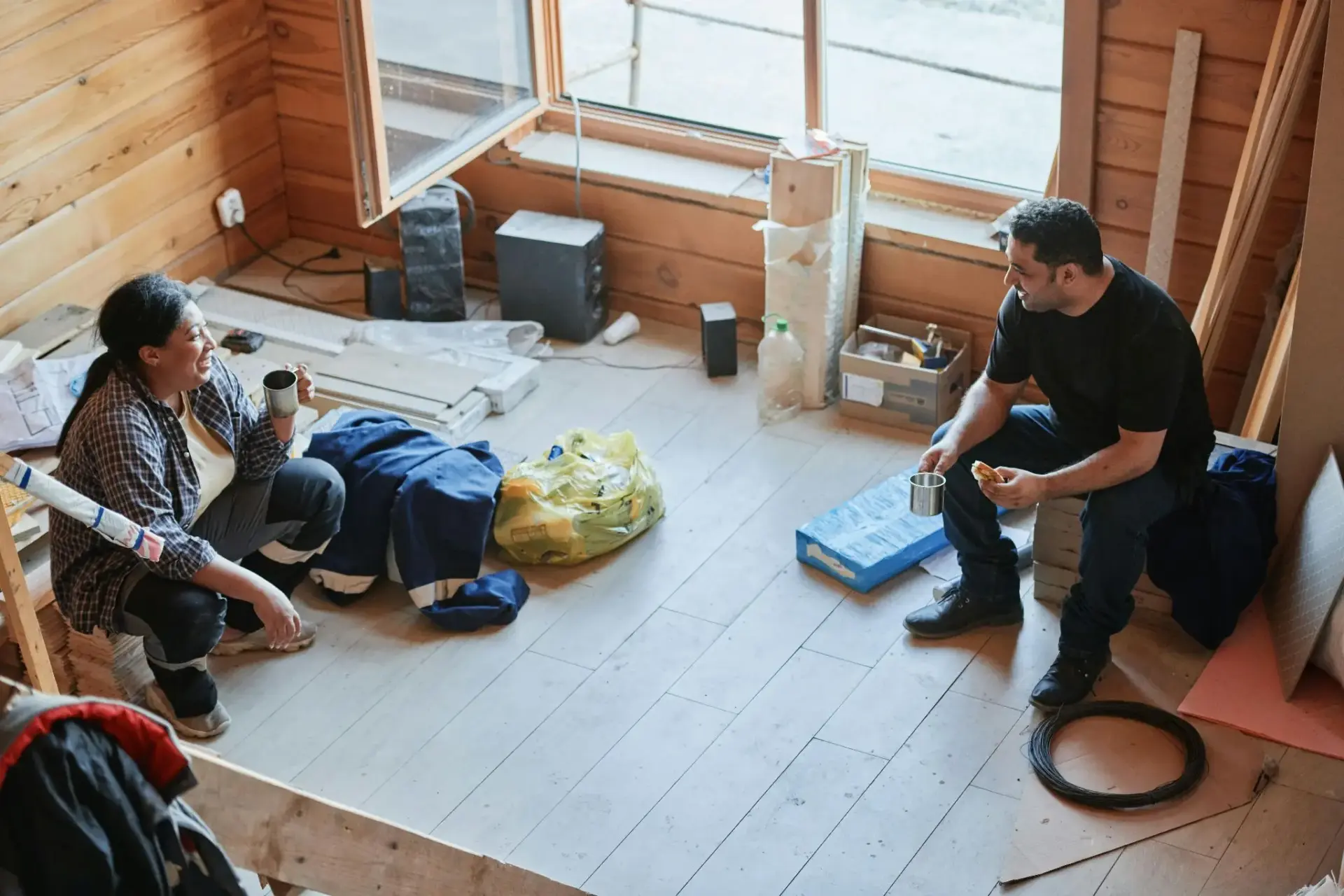 Two people taking a break in a partially renovated wooden room with tools and materials scattered around