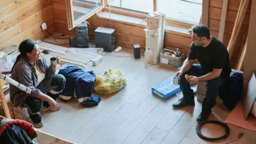Two people taking a break in a partially renovated wooden room with tools and materials scattered around