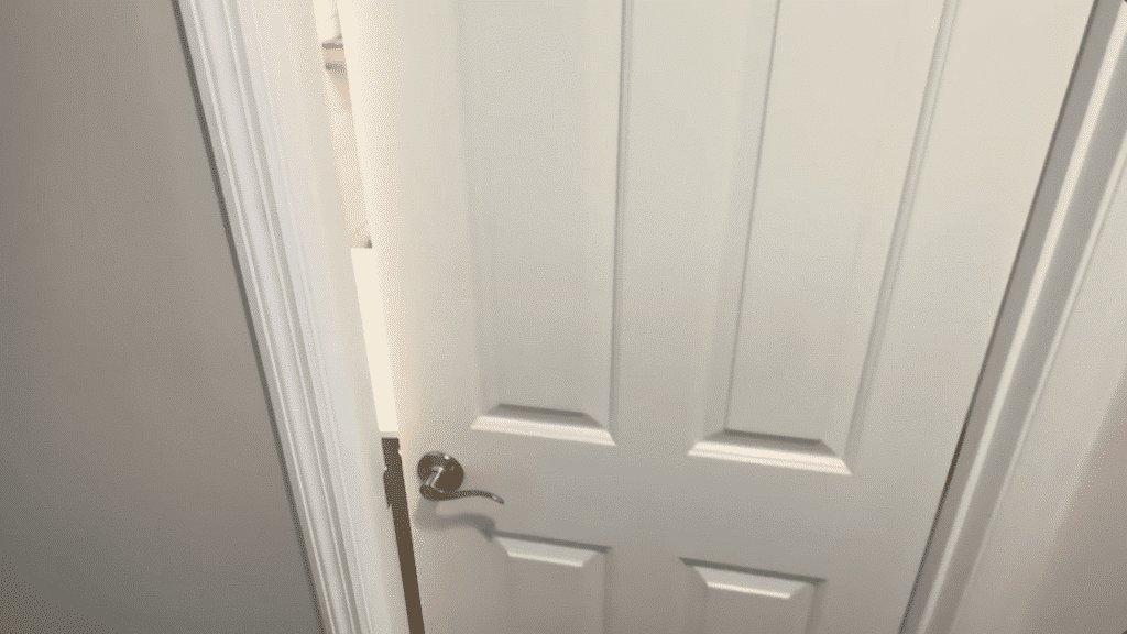 the image shows a partially opened white door with a round silver handle, revealing a bathroom interior behind it.