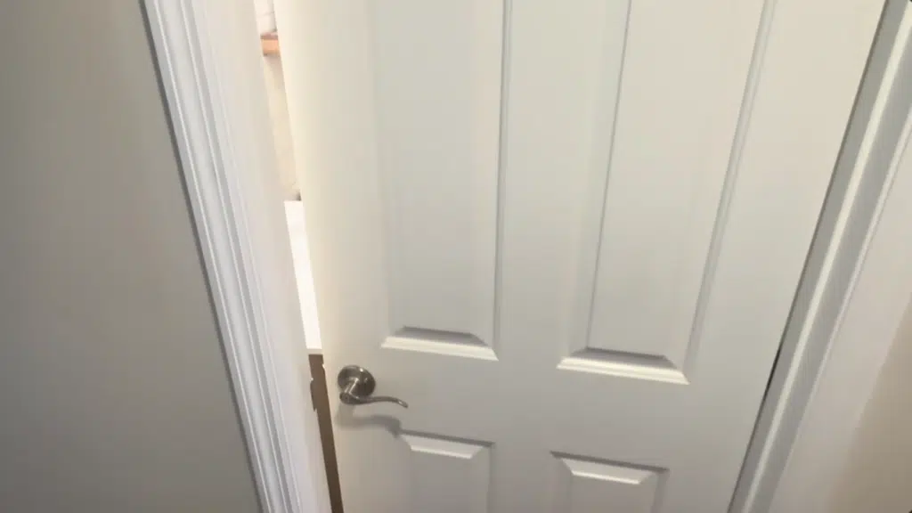 the image shows a partially opened white door with a round silver handle, revealing a bathroom interior behind it.