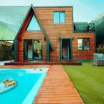 Modern wooden cabin with A-frame design, poolside seating, and artificial turf yard