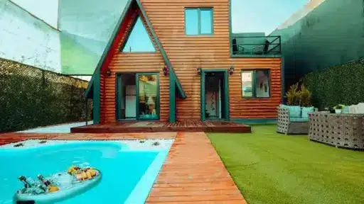 Modern wooden cabin with A-frame design, poolside seating, and artificial turf yard