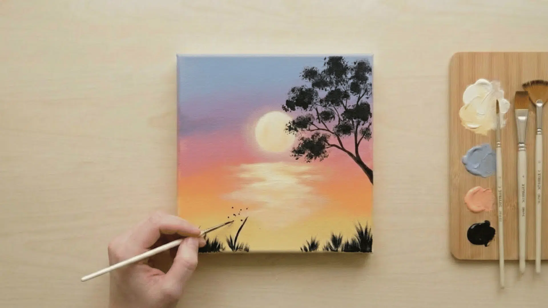 top view of finished beginner acrylic sunset painting with hand adding final grass details