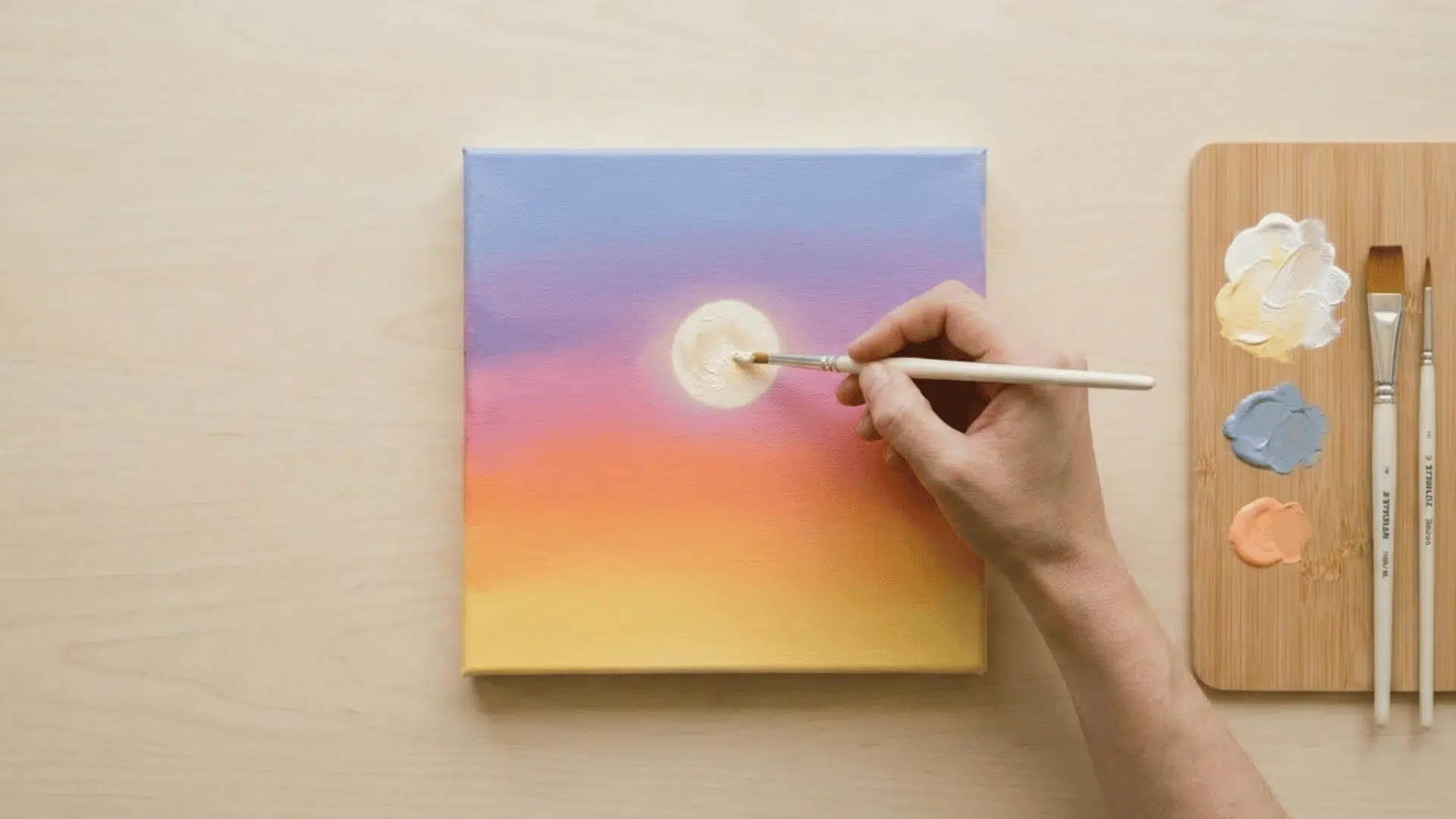 top view of hand adding moon on sunset painting using white paint with palette nearby