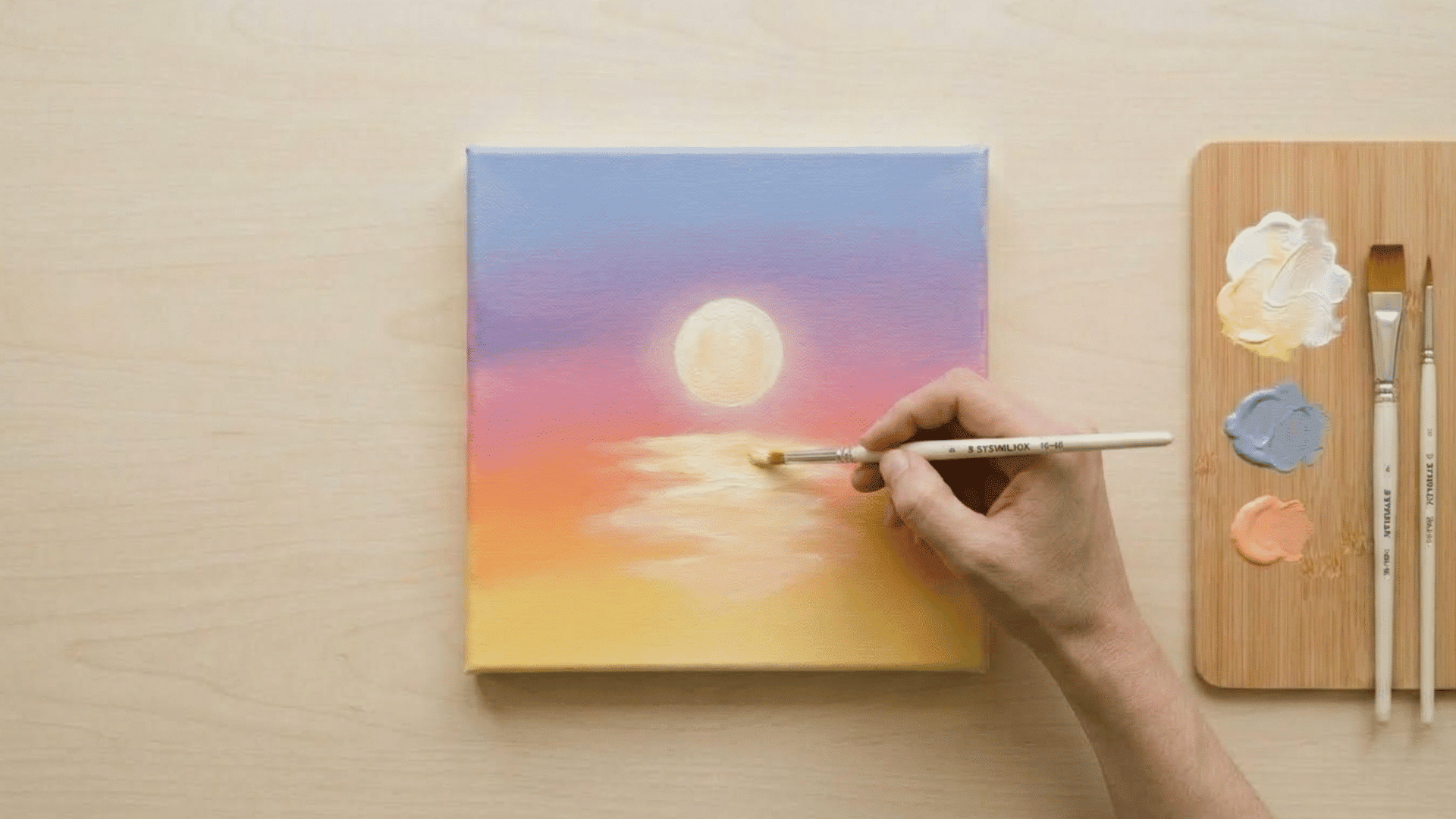 top view of hand blending water reflection in sunset painting with soft brush strokes