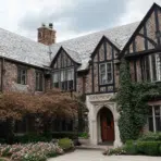 tudor revival house exterior with steep roof half timbering brick walls and arched entry surrounded by greenery