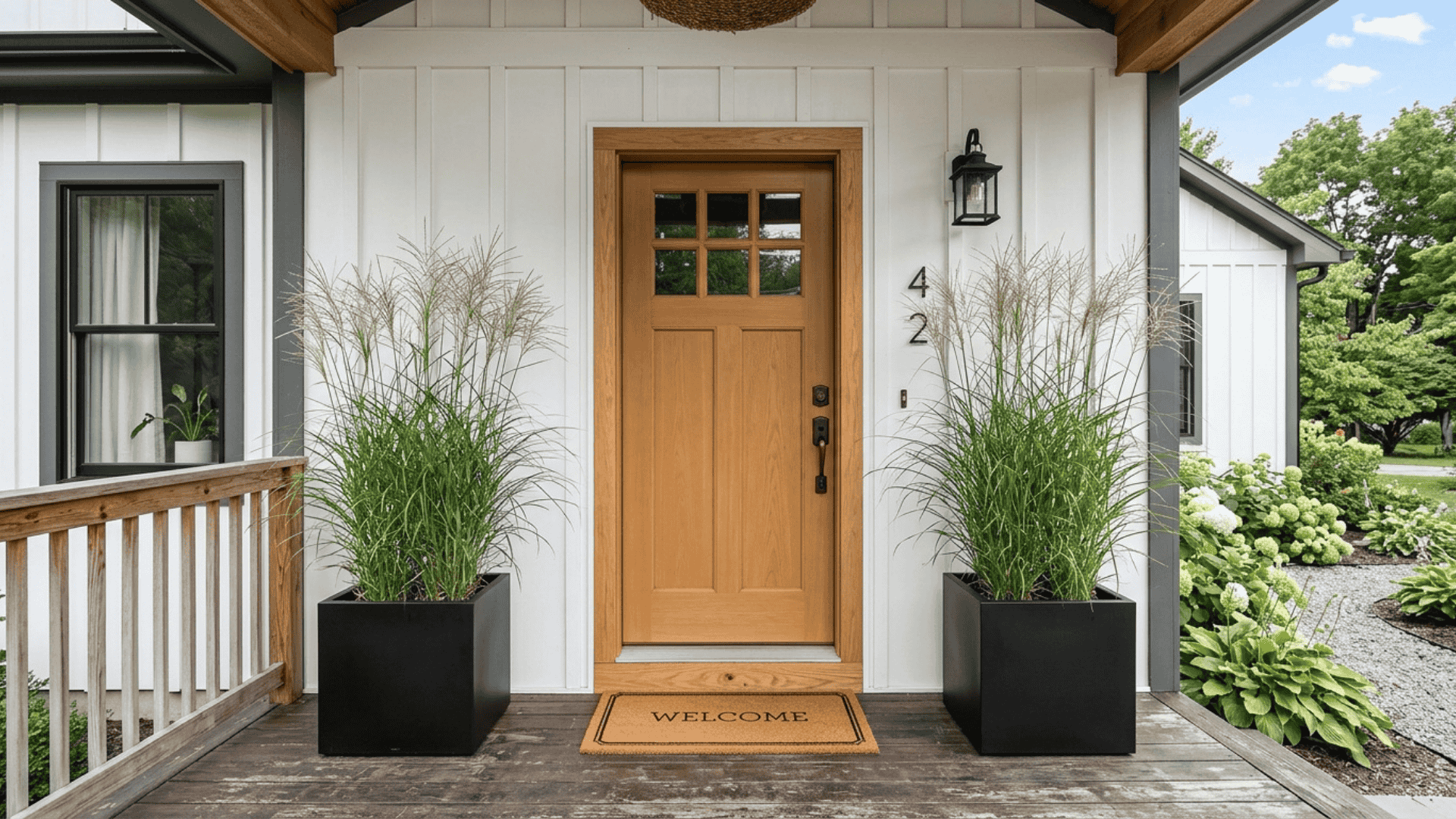 two matching black square planters with tall grasses framing a white farmhouse front door