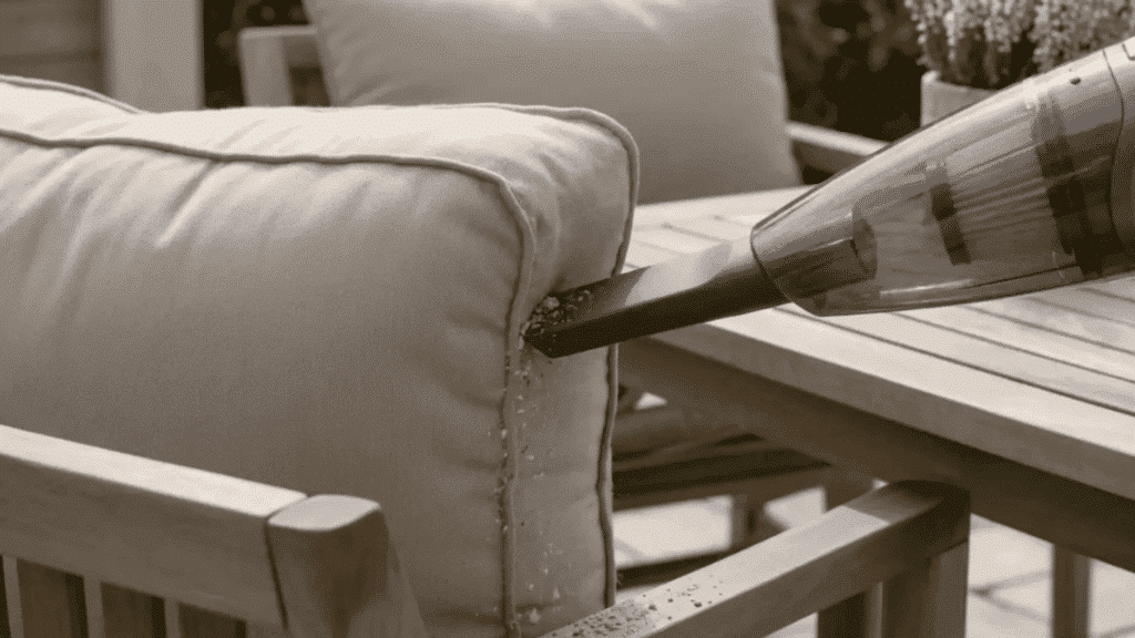 vacuum nozzle cleaning dirt from outdoor cushion seam on patio furniture.