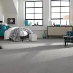 Modern bedroom with gray carpet, teal armchair, and geometric-patterned bedding in natural light