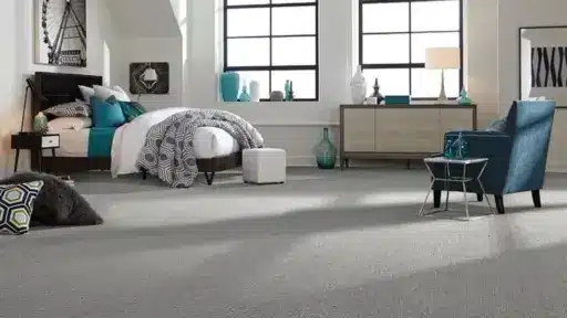 Modern bedroom with gray carpet, teal armchair, and geometric-patterned bedding in natural light