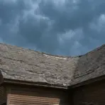 Old wooden house with weathered roof under stormy sky