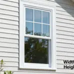 white framed double hung window on light siding exterior wall with visible trim and reflected trees in glass panes