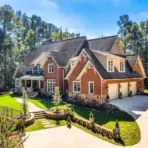 Large brick house with gabled roof and manicured lawn in wooded suburban setting