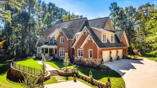Large brick house with gabled roof and manicured lawn in wooded suburban setting