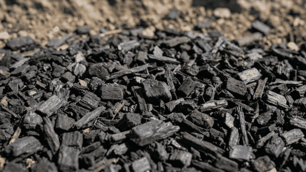 Black rubber mulch pieces covering outdoor ground surface with rough texture, natural sunlight, and realistic close-up landscaping detail.