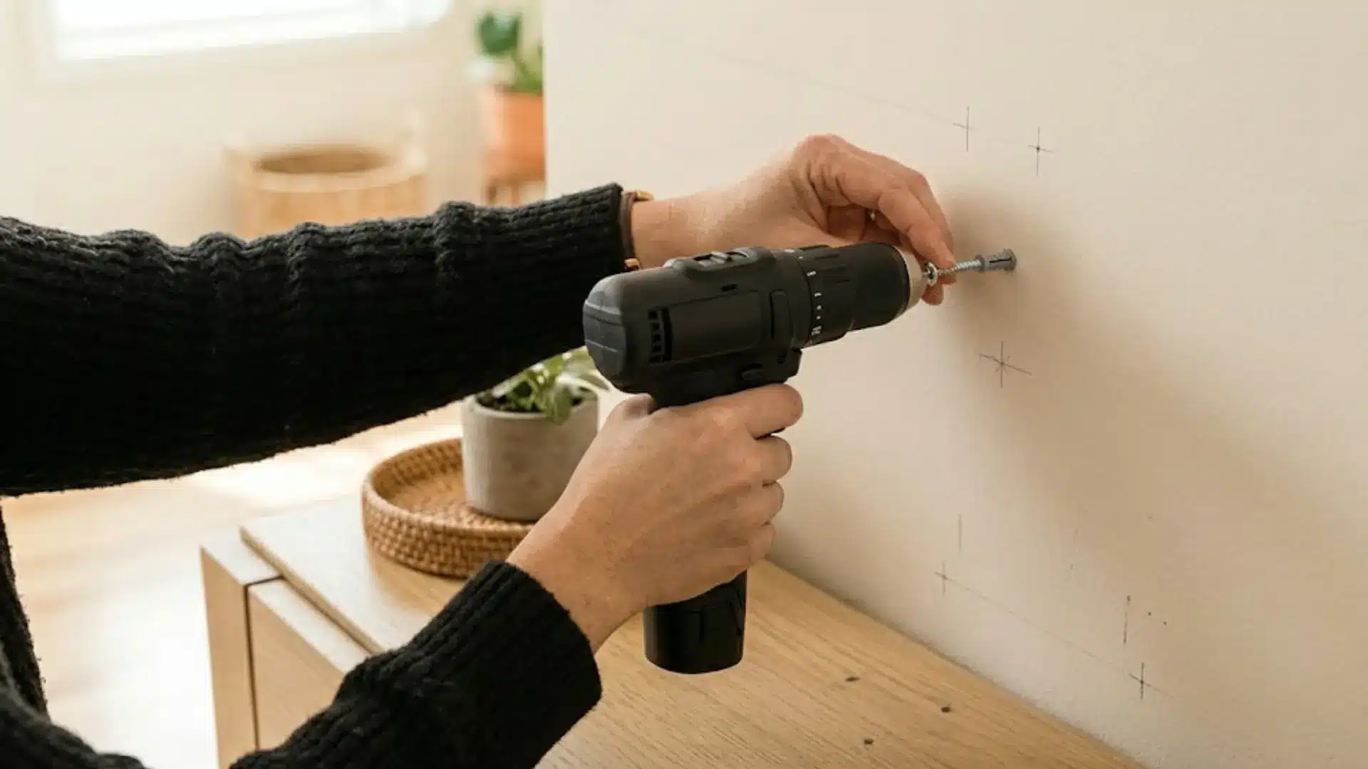 a close-up view of a power drill in use, drilling a pilot hole and setting an anchor into a marked section of the wall