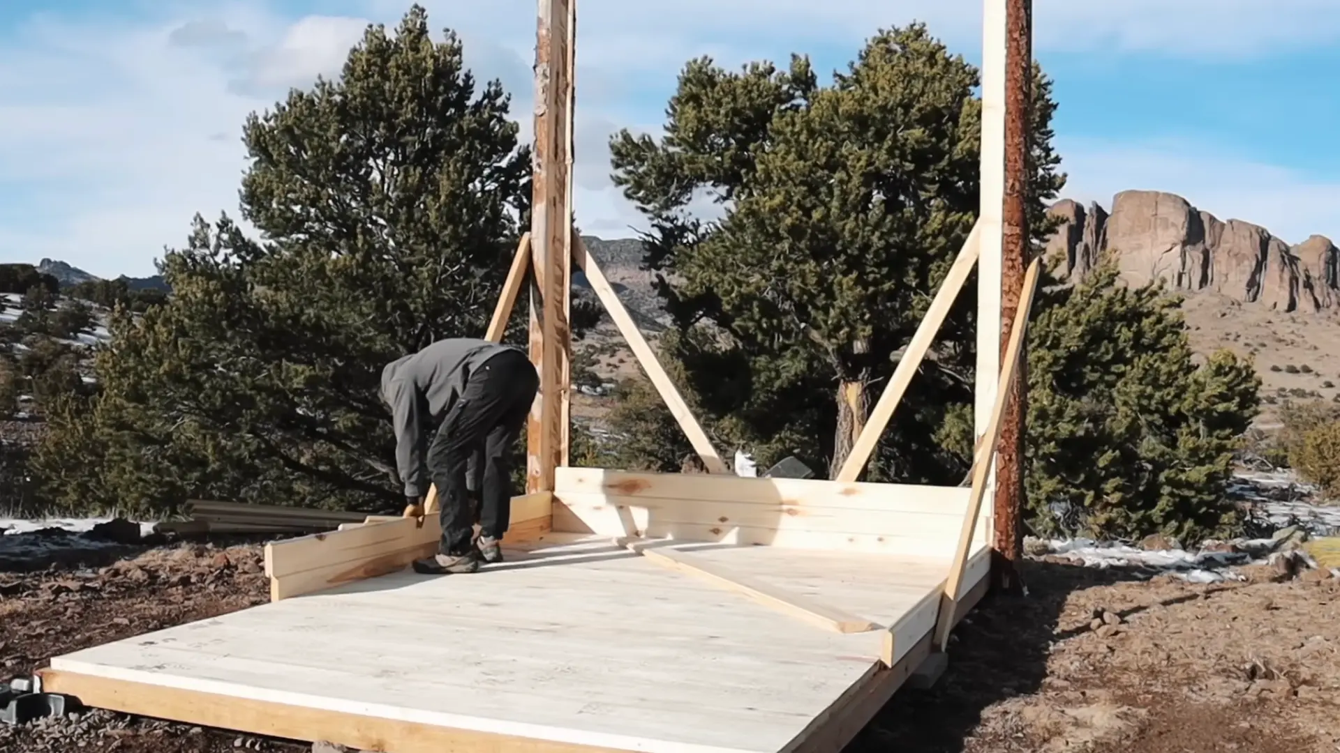 a person assembling a wooden post and beam frame structure on a flat tongue and groove floor base for a diy sauna build (1)