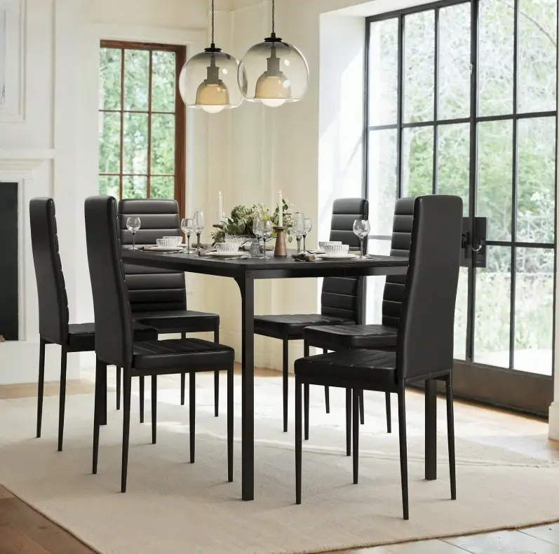 Black dining chairs around a set table in a bright dining room with glass pendants